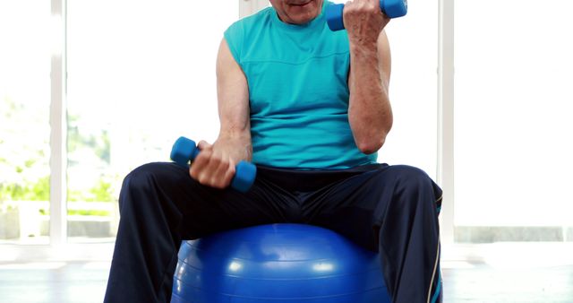 Senior man engaging in strength training while sitting on a stability ball at home. Perfect for promoting active lifestyle, senior fitness, home exercise routines, and health and well-being for older adults.