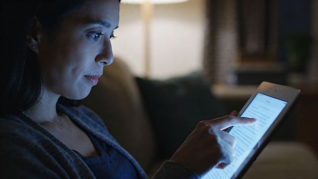 Woman reading on tablet at night touching screen on sofa for evening relaxation blue-light