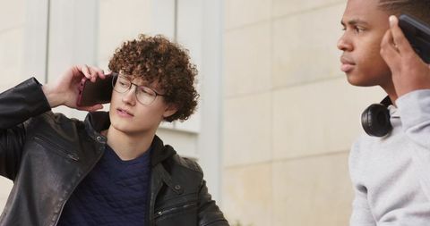 Diverse young men talking on smartphones near stone facade casual urban lifestyle