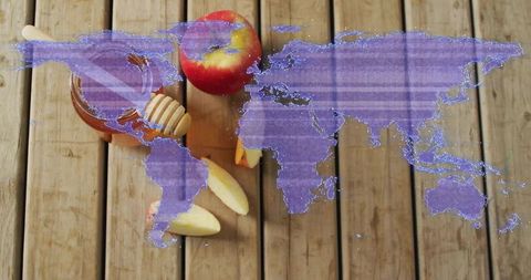 Rustic honey jar with dipper and apple slices on wooden table with purple world map