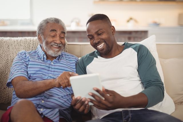 Smiling father and son using digital tablet in living room at home