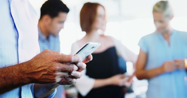 The photo shows three business professionals in an office environment, focusing on their mobile devices. This illustrates modern workplace dynamics. Ideal for use in business and technology contexts, presentations, articles on office culture and teamwork, or marketing materials emphasizing collaboration and connectivity.