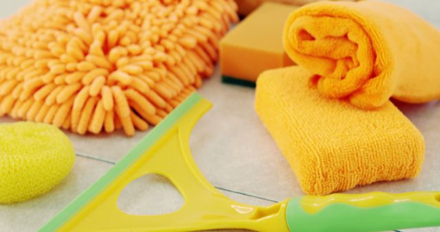 Various cleaning supplies including yellow cloth, orange sponges, squeegee, and microfiber cloth displayed on a tile floor. Useful for illustrating cleanliness, home maintenance, and domestic chores in articles, blogs, and advertisements. Perfect for cleaning and hygiene-related content.