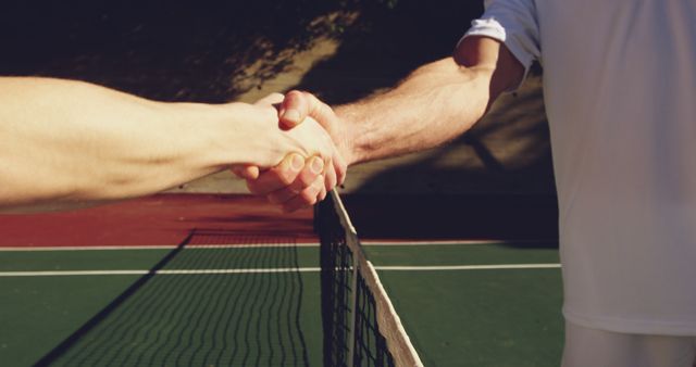 Two people are shaking hands over a tennis net, signaling sportsmanship after a match. Their handshake represents the respect and camaraderie that is often found in competitive sports.