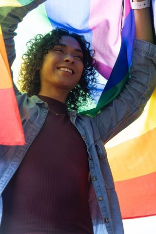 Nonbinary adult holding rainbow pride flag under sunlight celebrating joyful lgbtq+
