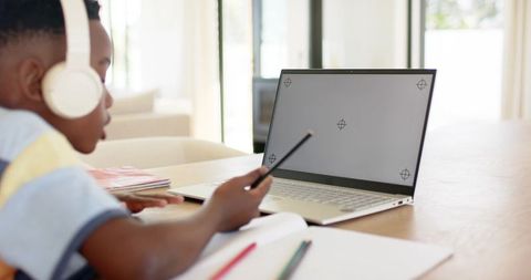 African american child studying at home pointing pencil at laptop with headphones