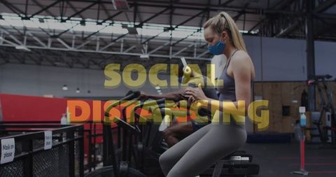 Woman Wearing Mask Using Smartphone on Exercise Bike in Gym