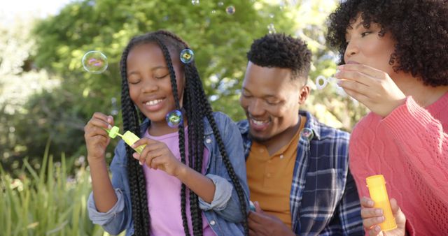 Happy african american parents with daughter blowing bubbles in garden at home. Domestic life, nature and lifestyle, unaltered.