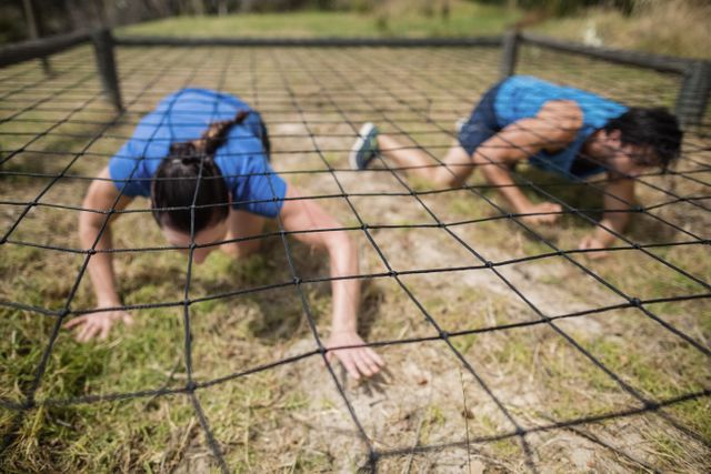 Fit man and woman crawling under the net during obstacle course in boot camp