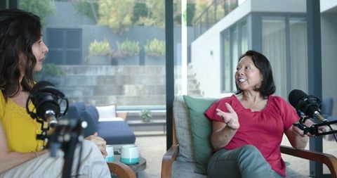Diverse female cohosts interviewing senior asian guest on cozy home patio live podcast