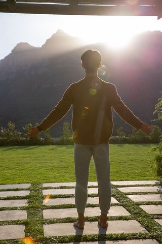 Man embracing sunrise on mountain patio with backlit silhouette and lens flare