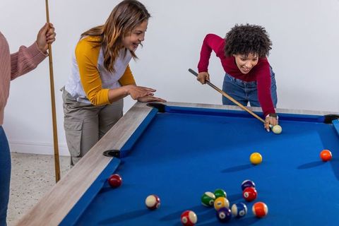 Multiracial friends playing pool, lining up shot on blue felt table during game night