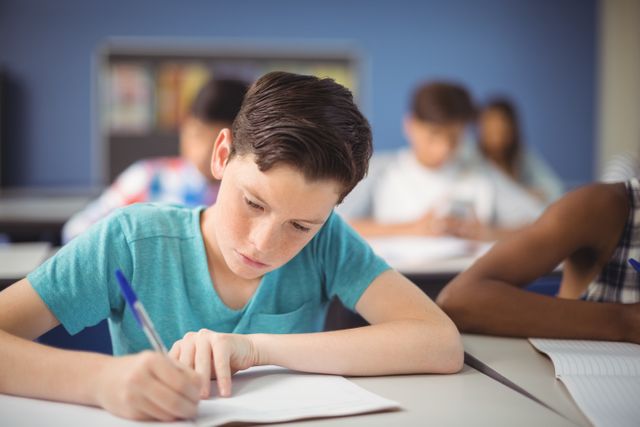 Young boy concentrating on writing in a classroom setting. Ideal for educational materials, school-related advertisements, and articles about childhood education and learning environments.