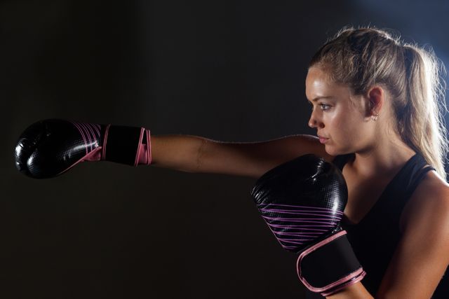 Woman wearing boxing gloves practicing punch in fitness studio. Excellent for fitness and sports advertising, motivational posters, health and wellness blogs, women's empowerment visuals, and athletic training resources.