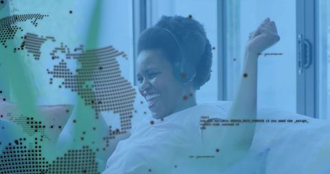 Laughing woman wearing headphones on sofa with digital world map and code overlay