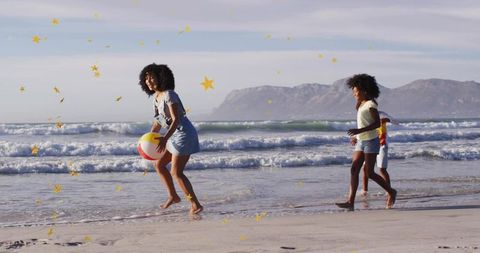 Black family playing on sunlit beach holding beach ball with golden star confetti