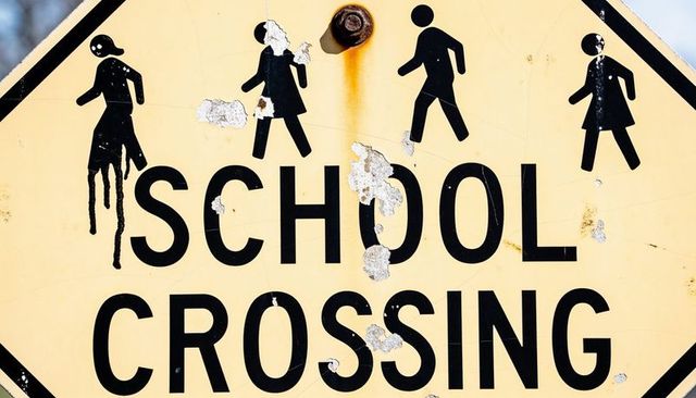 Showing worn school crossing sign with peeling paint and weathered pedestrian icons