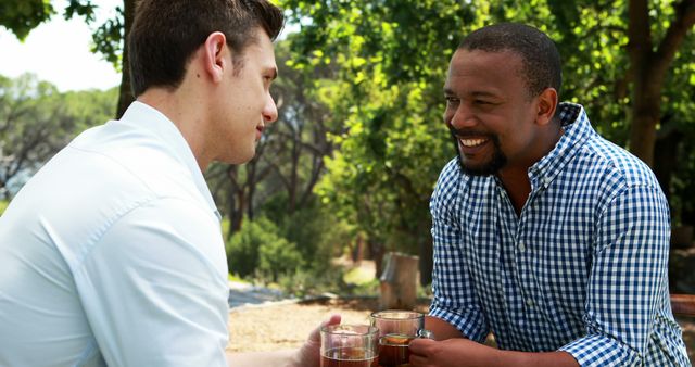 Two friends of different ethnicities enjoying a conversation outside, holding beverages. The atmosphere is casual and joyful. Suitable for depicting friendship, social interactions, bonding moments, outdoor activities, or leisure time.