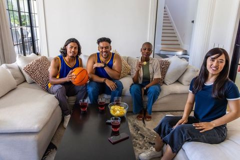 Friends watching basketball at home wearing matching jerseys, enjoying snacks and drinks