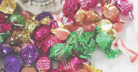 Glistening heap of assorted foil-wrapped candies and gummy pieces on white tabletop