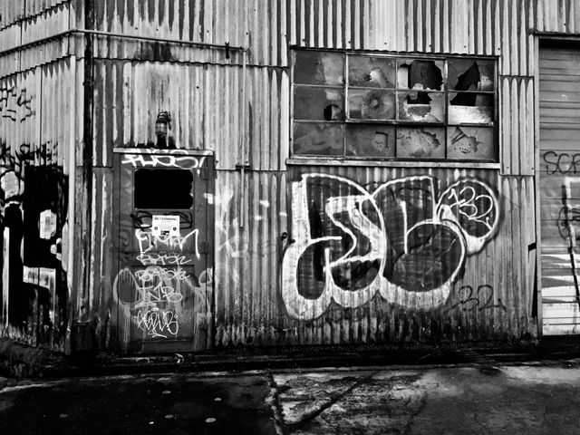 Wall with vibrant graffiti and old industrial building shows abandonment and urban decay. Suitable for themes of urban exploration, societal issues, street art culture, and the contrast between decay and art.