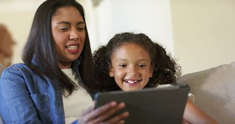 Mother and Daughter Bonding over Tablet on Couch Laughing and Learning Together