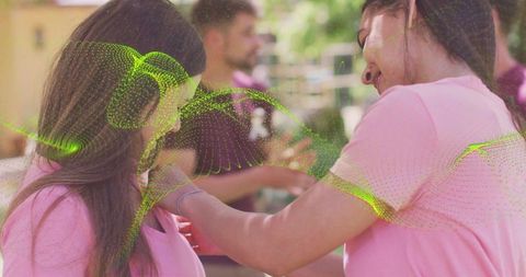 Volunteers fastening lanyards and sharing smiles at outdoor charity event in pink tees