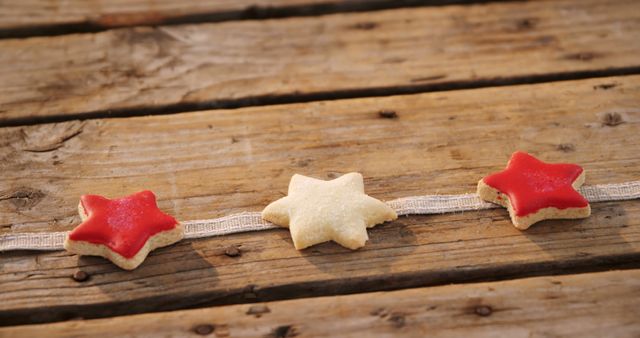 Three star-shaped cookies, two red and one white, are placed in a row on a rustic wooden table. The vibrant colors and the weathered wooden background create a festive and warm ambiance. This image can be used for holiday baking blogs, festive season promotions, or cookbooks featuring dessert recipes.