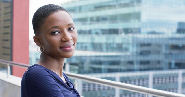 African woman leaning on balcony with cityscape background. Her confident expression and professional attire make this ideal for business or corporate content, websites, or advertisements targeting urban professionals. Perfect for showcasing a fresh, modern, and positive environment.