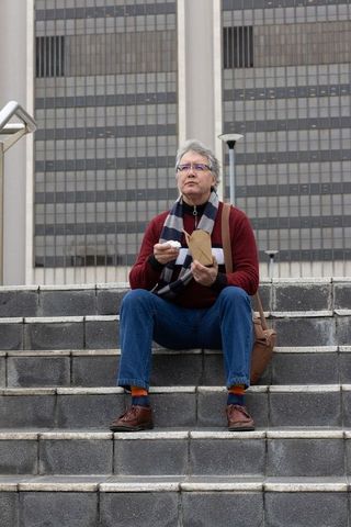 Middle-aged man sitting on city steps eating takeout with scarf and messenger bag