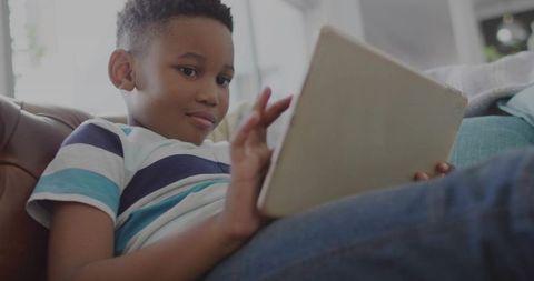 School-age boy reclining on leather couch using tablet for learning, reading and play