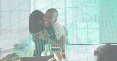 Colleagues celebrating success hugging at office desk with teal data overlay and charts