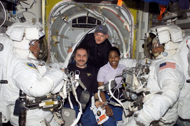 Shows five members of the STS-121 crew on the International Space Station. The group includes astronauts and a cosmonaut preparing for a spacewalk in the Quest Airlock, wearing Extravehicular Mobility Unit spacesuits. Suitable for articles and educational content about space missions, international collaboration in space, or photo collections related to space exploration.