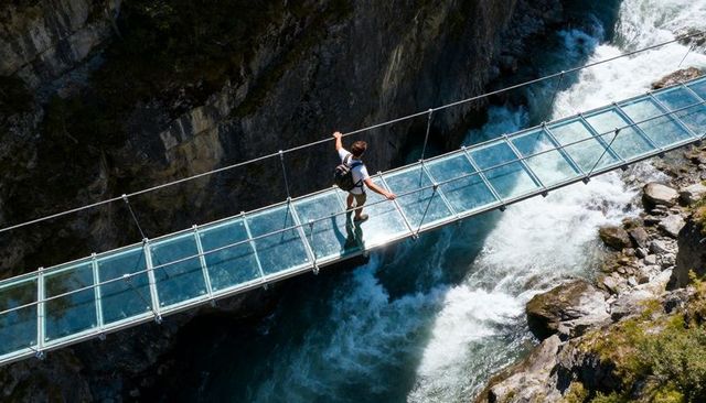 Hiker crossing glass-bottom suspension bridge above mountain gorge and rushing river