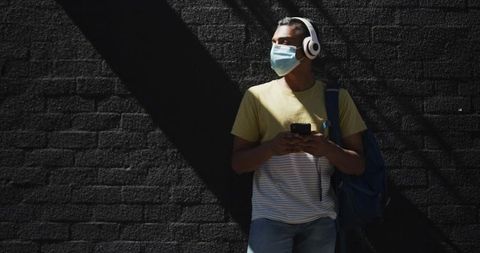 Man Wearing Mask and Headphones Using Smartphone