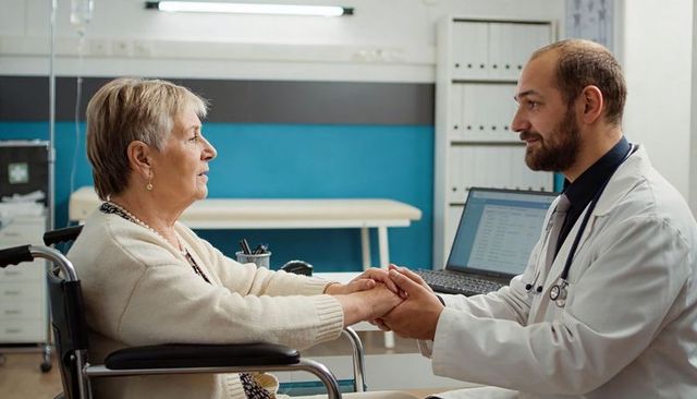 Doctor holding hands with senior woman in wheelchair compassionate medical consultation