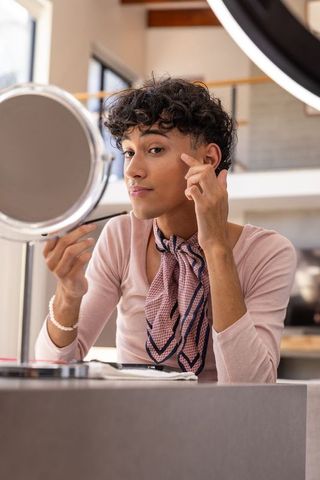 Young man applying eye makeup in well-lit loft area