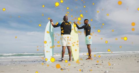 Holding surfboards on sandy beach with glowing orange bokeh particles and ocean waves