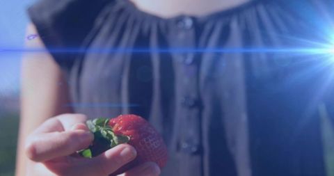 Young girl offering fresh strawberry in sunlight with lens flare and bokeh