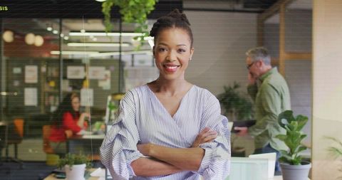 Female manager standing with arms crossed in bright modern open-plan office leading team