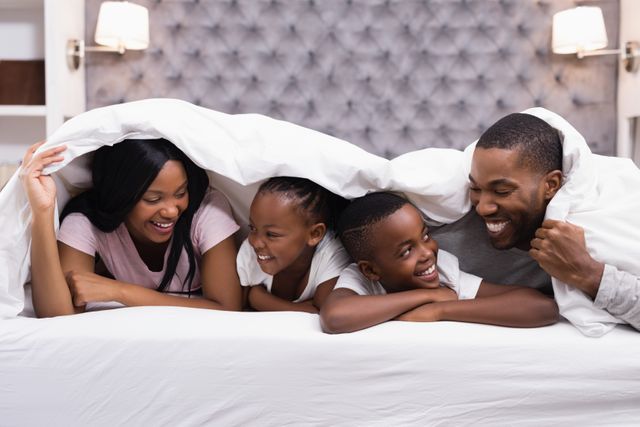 Happy family lying together under blanket on bed at home