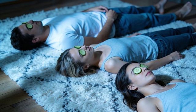 Three adults lying on shag rug relaxing during at-home spa night with cucumber eye masks