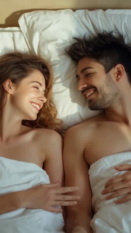 Vertical video: Couple waking, smiling, reaching hands under white sheet for intimate morning