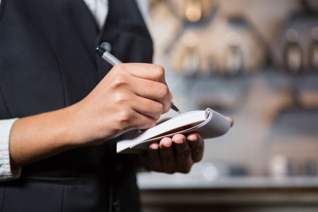 This image depicts a bartender writing down an order in a bar. It is useful for illustrating concepts related to hospitality, customer service, and professional work environments. Ideal for use in articles, blogs, or advertisements focusing on the restaurant industry, service jobs, or training materials for hospitality staff.