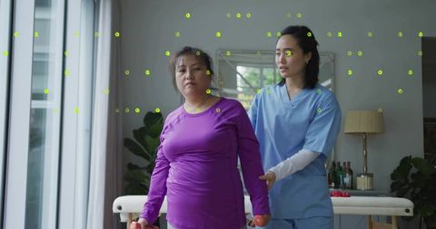 Korean woman walking with hand weights during supervised rehab session with therapist in bright room