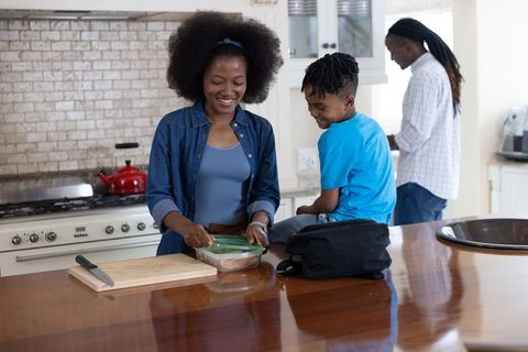 African american mother preparing packed lunch on kitchen island with smiling son