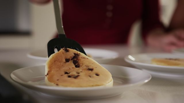 Woman serving freshly made blueberry pancakes on plates in home kitchen. Great for content related to homemade breakfast recipes, domestic life, cooking tutorials, and morning routines.