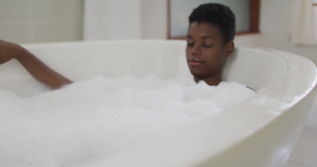 Young man enjoying a peaceful bubble bath, showcasing relaxation and self-care at home. Ideal for wellness blogs, lifestyle articles, ads promoting relaxation products, or content related to stress relief and mental health. Highlights themes of tranquility and personal care routines.