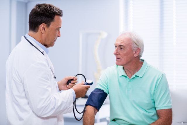 Doctor measuring blood pressure of elderly male patient in a clinical setting. Useful for healthcare, medical services, senior care, and wellness-related content. Ideal for illustrating doctor-patient interactions, medical checkups, and health assessments.