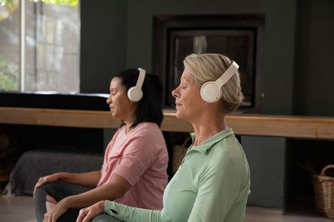 Mature women meditating with headphones in sunlit wellness studio practicing mindfulness